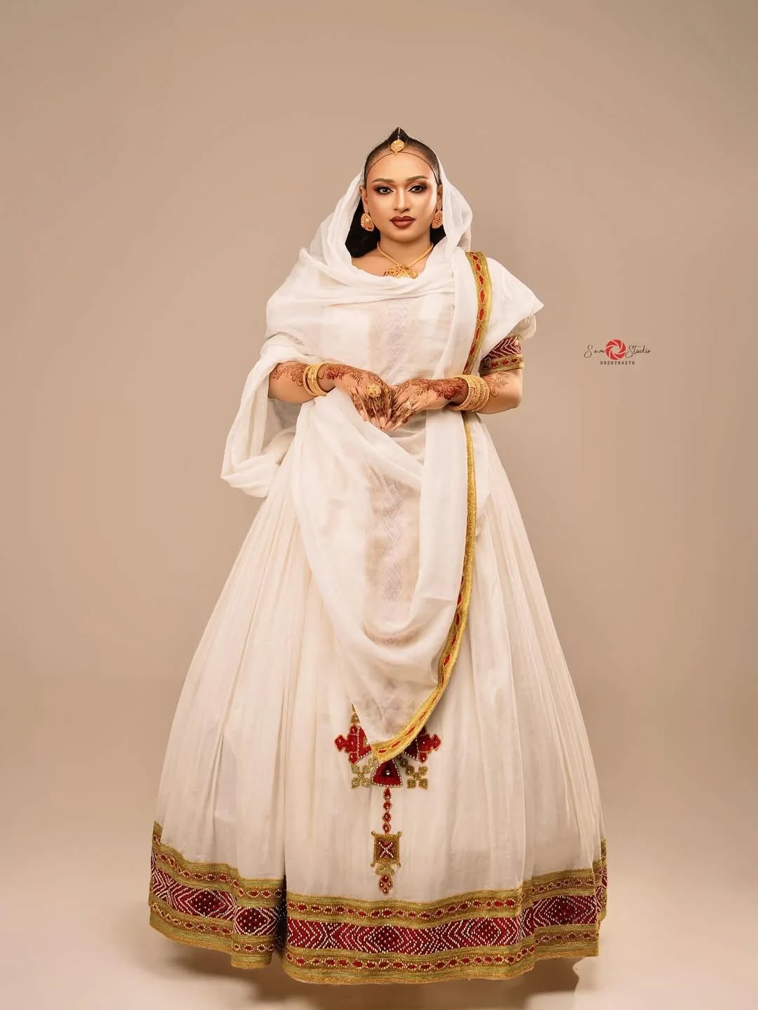 Woman wearing a traditional white outfit with gold and red details on a beige background