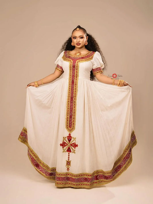 Woman wearing a white dress with red and gold embroidery on a beige background