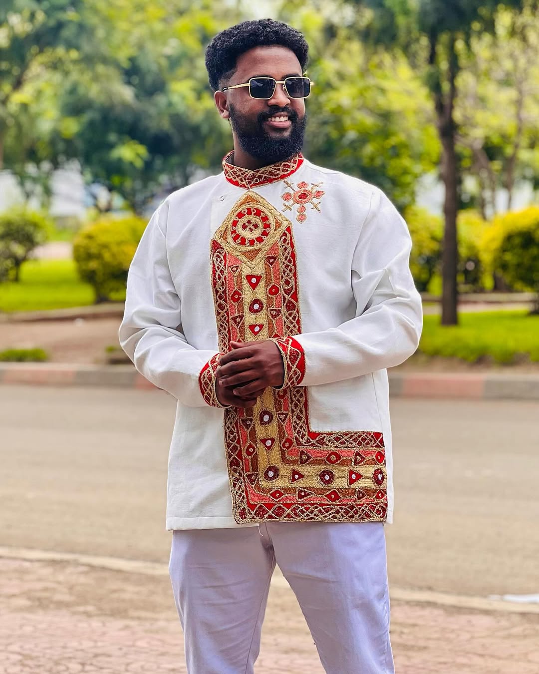 Man wearing a traditional embroidered outfit with sunglasses outdoors. Traditional Habesha Men’s Clothing | New Ethiopian & Eritrean Attire Ethgebya