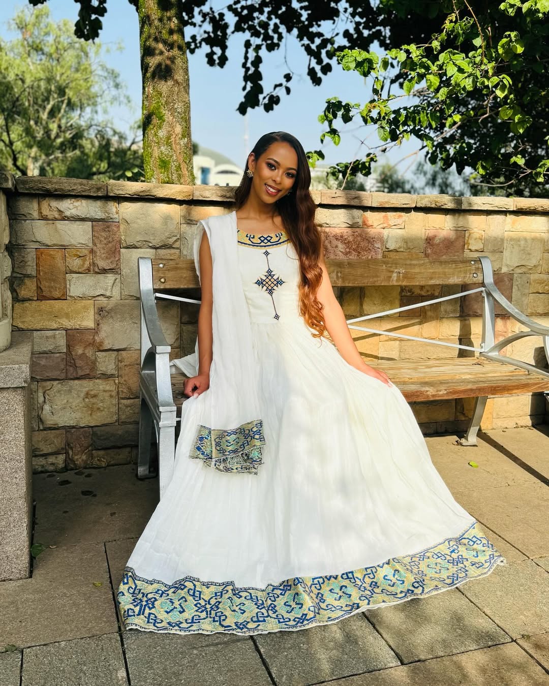 Woman in a white dress with floral patterns sitting outdoors on a stone patio. Luxury Navy, Gold & Green Zuria Kemis