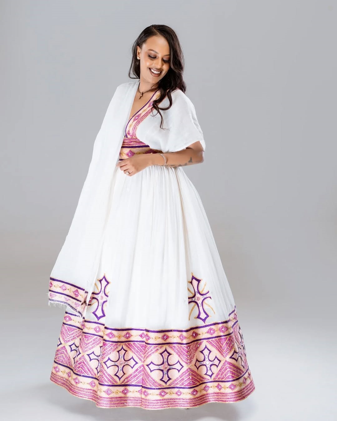 Woman wearing a white dress with pink and purple patterns on a gray background Rose Gold Modern Zuria Habesha Kemis Handcrafted Ethiopian Dress ethgebya gebeya usa