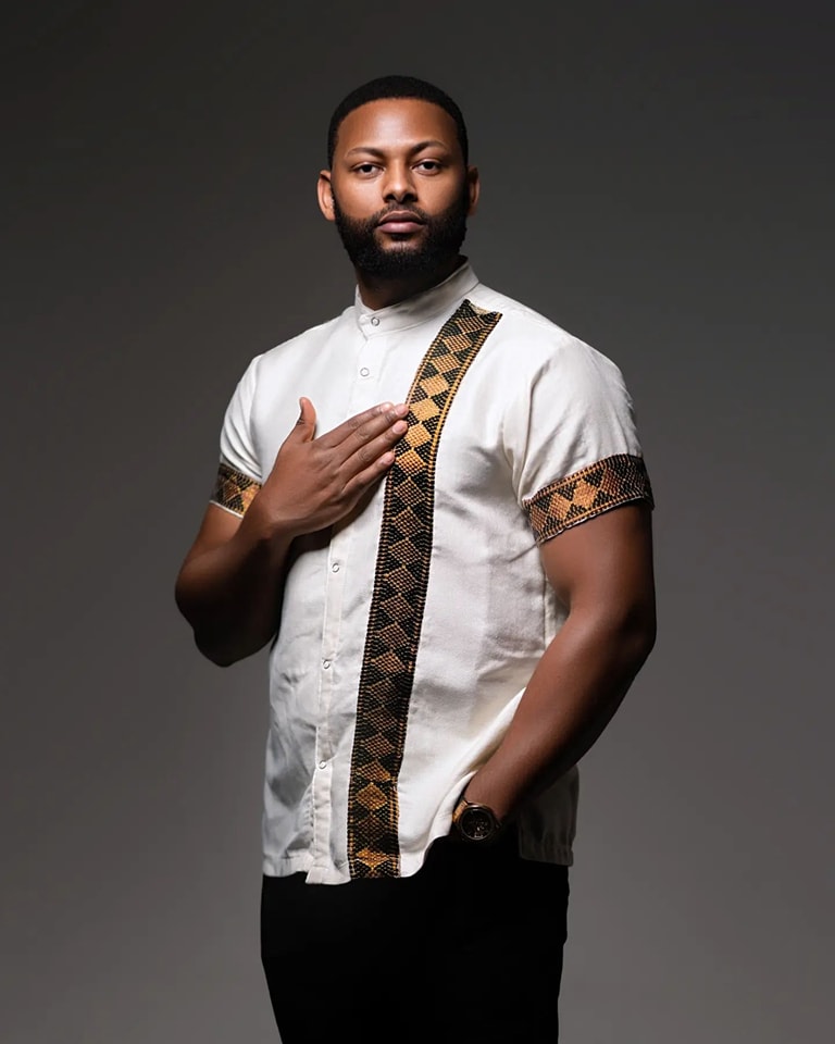 Man wearing a white shirt with black and gold patterns on a gray Modern Habesha Men’s Shirt Stylish Ethiopian Traditional Wearbackground