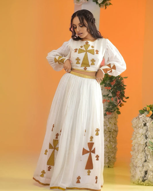 Woman wearing a white dress with gold and brown patterns against an orange background Golden Ethiopian Habesha Dress Handcrafted Zuria Kemis Set ethgebya gebeya usa zuria habesha kemis