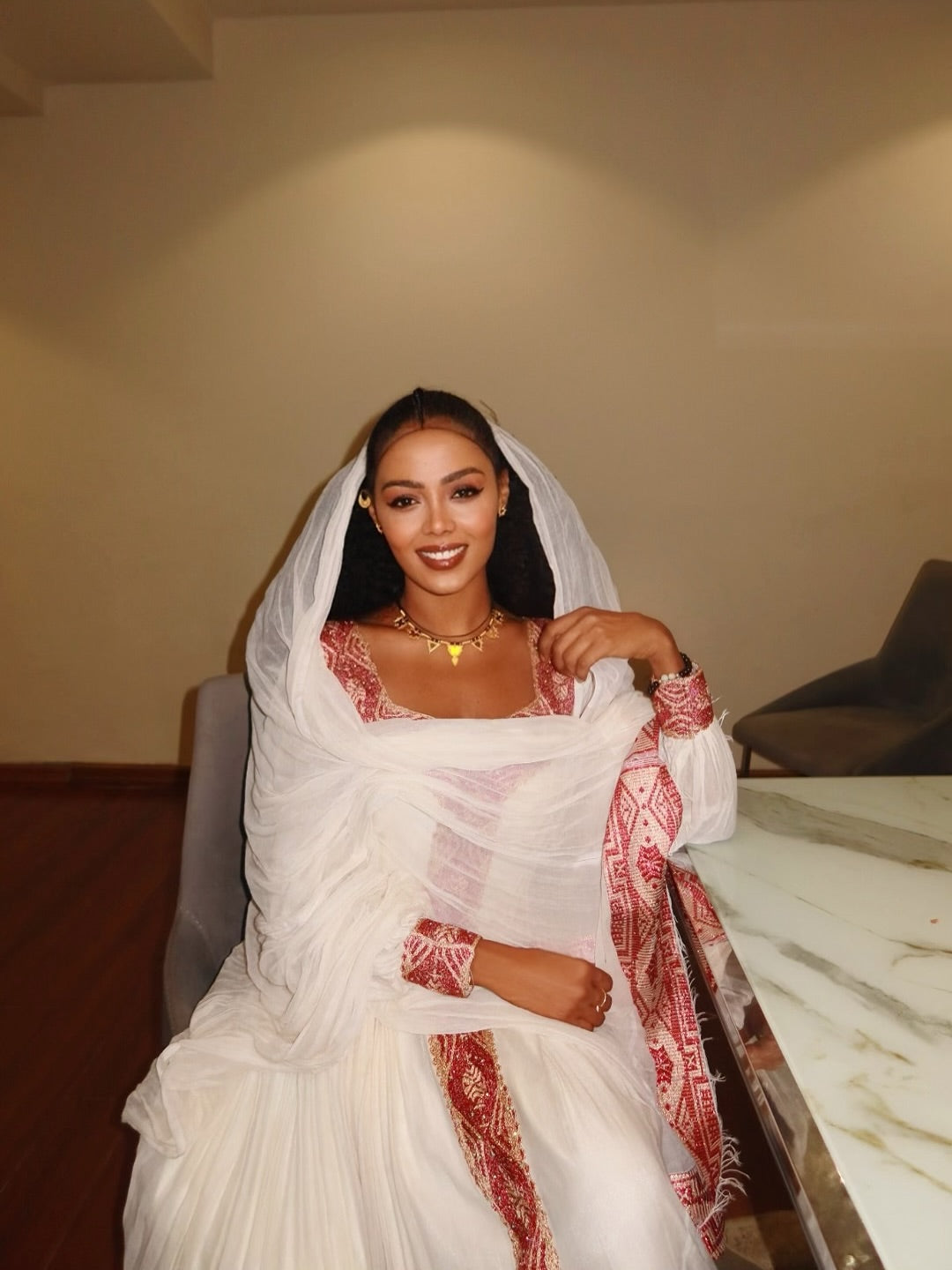 Woman in a white and red traditional outfit sitting indoors. New Pink Zuria Habesha Kemis Handcrafted Ethiopian Traditional Dress Ethiopia Gebebya Ethgebya
