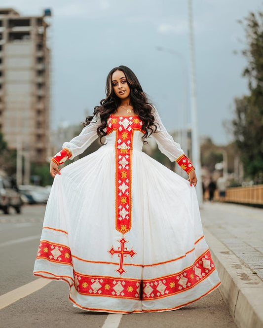 Woman wearing a white dress with red and gold embroidery on a street. Red Zuria Habesha Kemis New Modern Ethiopian Dress ethgebya gebeya usa habesha kemis