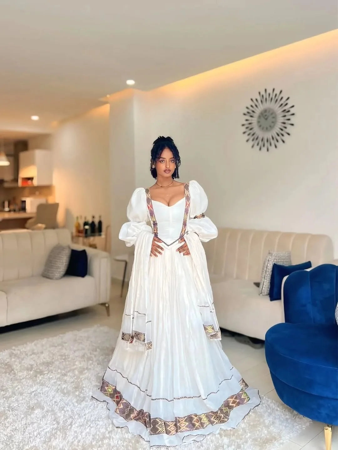 Woman in a white dress standing in a modern living room. One of a Kind Modern Zuria Kemis | Handcrafted Ethiopian Dress
