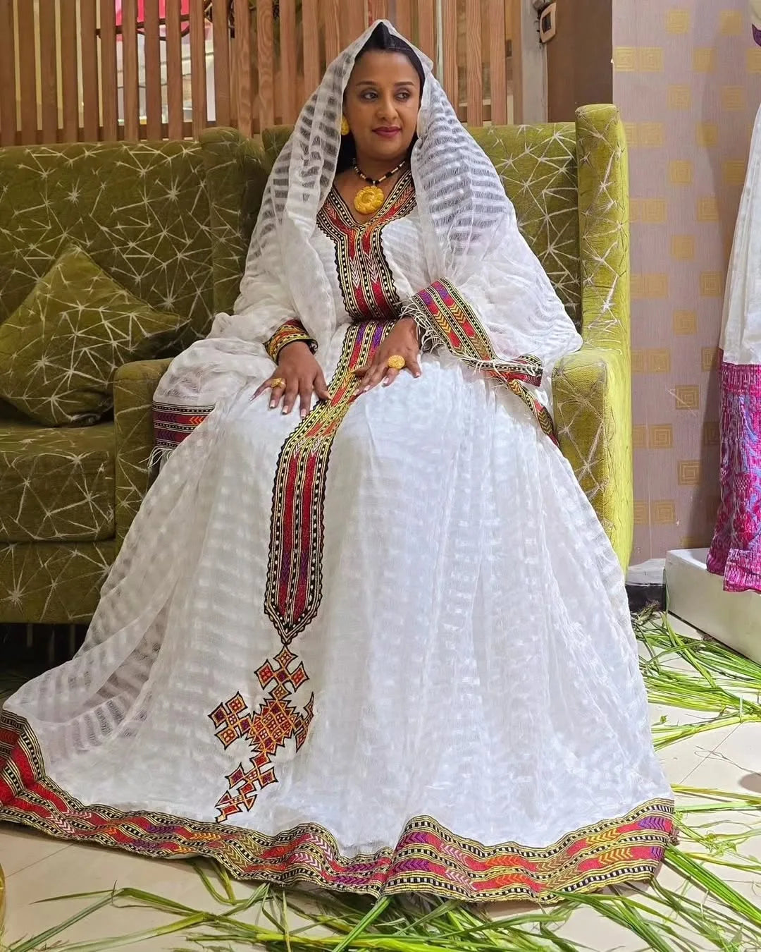 Woman in traditional embroidered outfit sitting on a green sofa. Elegant Zuria Habesha Kemis New Modern Ethiopian Traditional Dress ethgebya gebeya