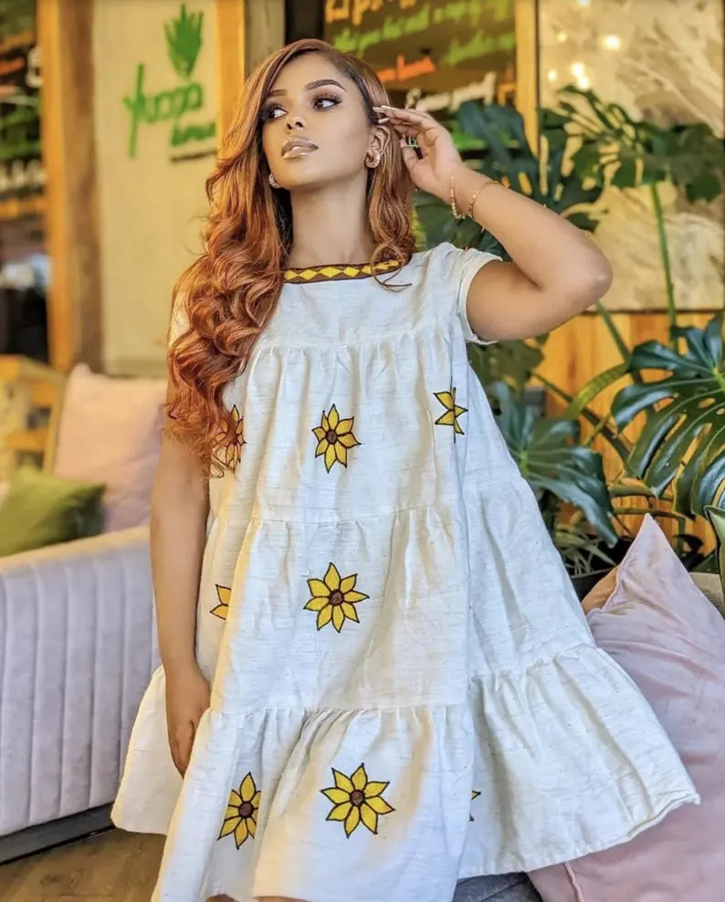 Woman wearing a white dress with yellow floral patterns in an indoor setting. Lightweight Short Habesha Dress Modern Summer Ethiopian Kemis ethgebya gebeya habesha kemis usa