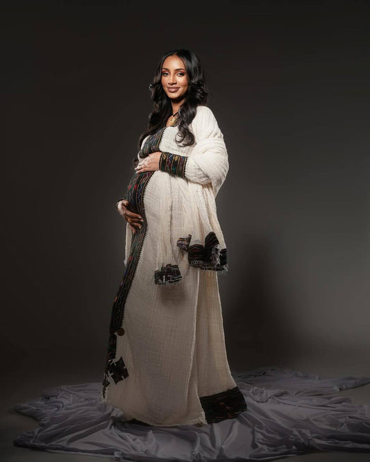 Pregnant woman in a long, light-colored dress with dark accents against a dark background Axum Habesha Kemis & Menβs White Shirt with Gabi Ethiopian Couple Set ethgebya gebeya usa habesha kemis men