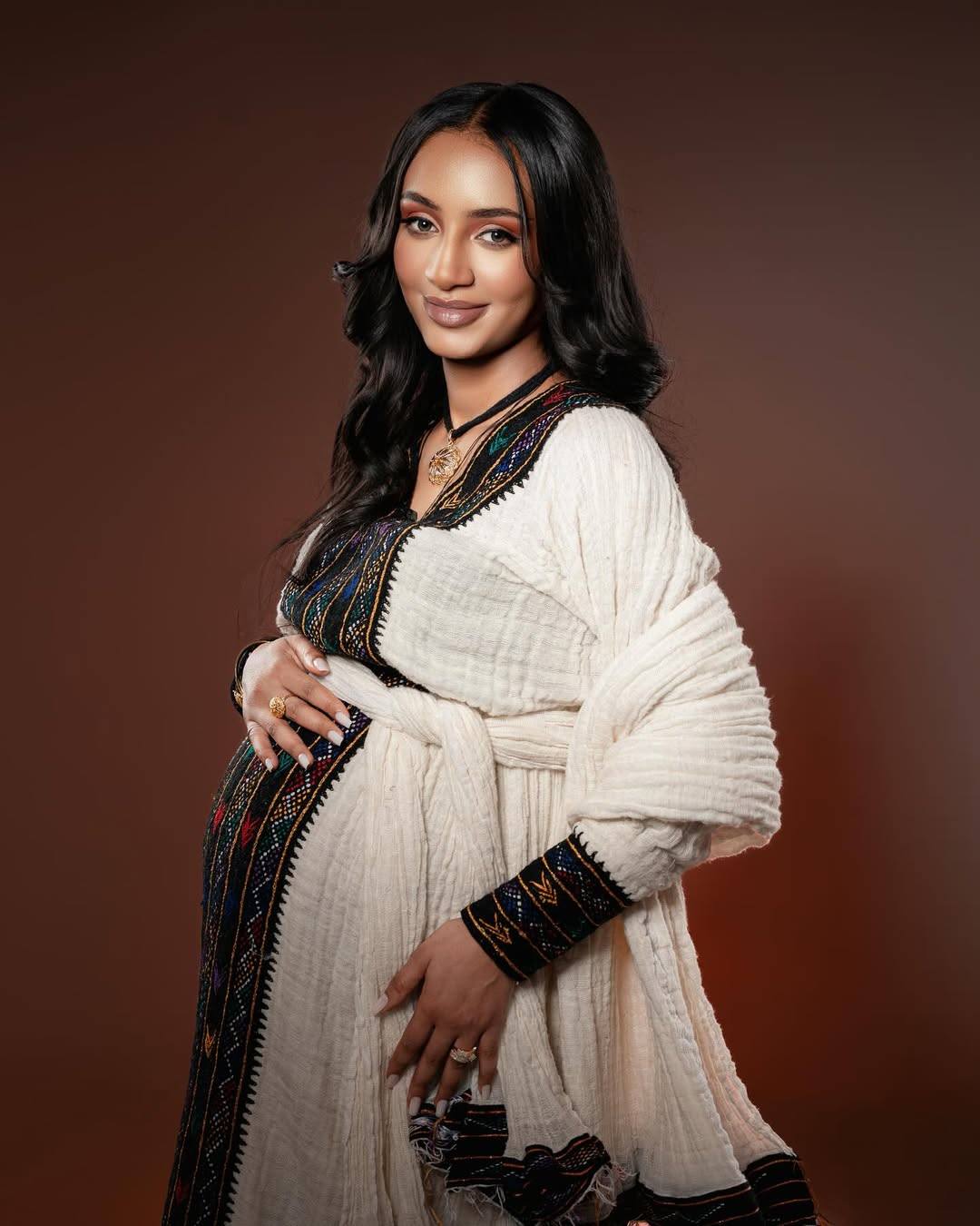 Woman wearing a traditional outfit with intricate designs on a brown background Axum Habesha Kemis & Men’s White Shirt with Gabi Ethiopian Couple Set ethgebya gebeya usa habesha kemis men
