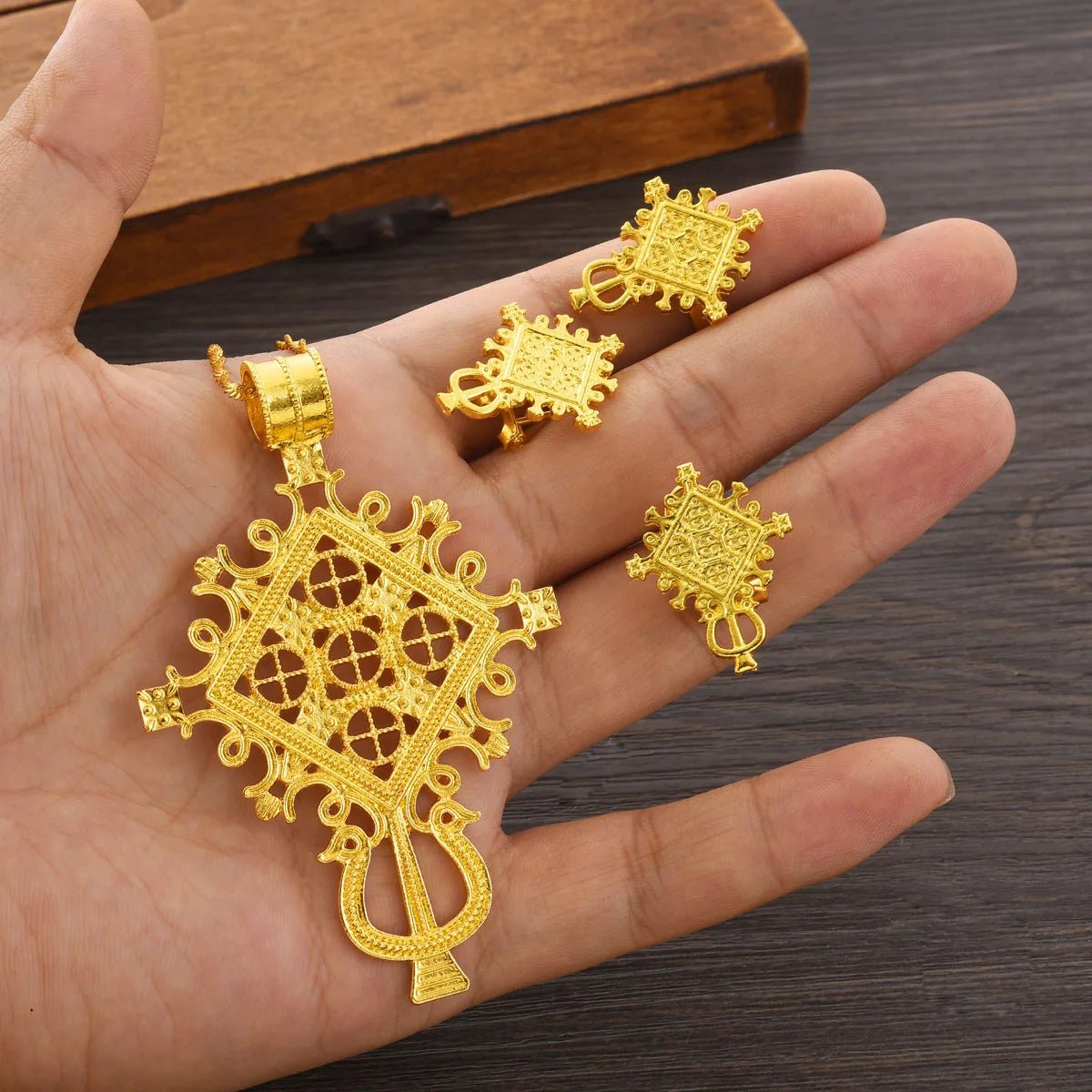 Gold jewelry set including a pendant and earrings on a hand against a wooden background