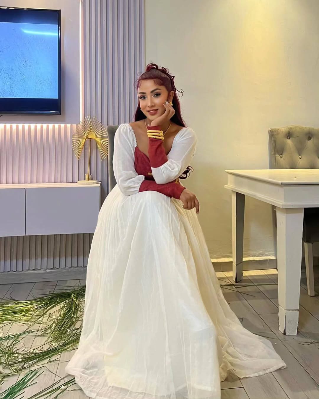 Woman in a white and red dress sitting in a modern living room. Elegant Modern Red-Accent Habesha Kemis Ethgebya