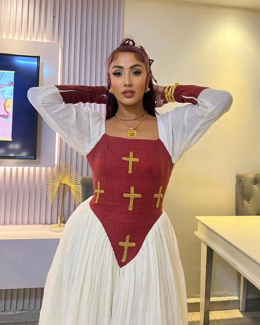 Woman wearing a red and white dress with gold crosses in an indoor Elegant  Modern Red-Accent Habesha Kemis Ethgebya setting.