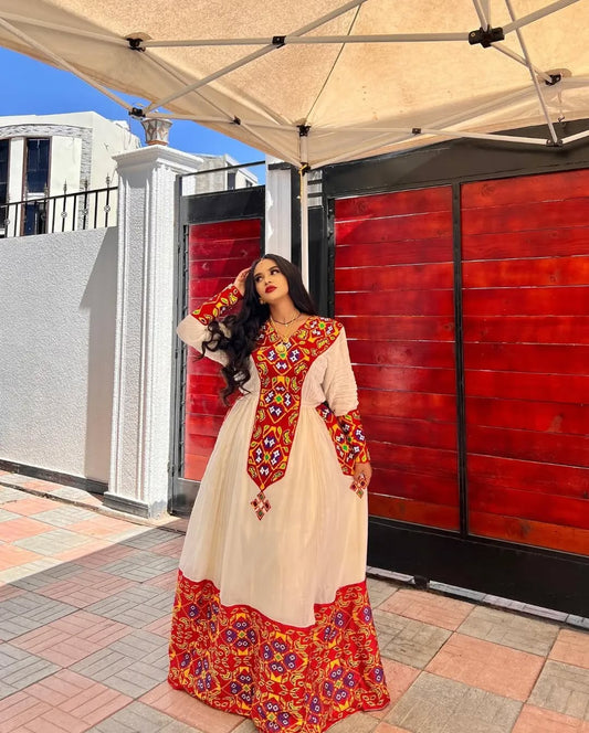 Woman in a traditional outfit with red and gold patterns standing outdoors. Stunning Red Zuria Habesha Kemis Handcrafted Ethiopian Dress  Ethiopian artisanal dress, Habesha style, Habesha fashion, Ethiopian cultural wear, Eritrean cultural attire, Habesha modern outfit, Ethiopian classic dress, Ethiopian embroidery fashion, Habesha traditional clothing, Ethiopian traditional outfits for women, Habesha chic dress, Ethiopian ethnic dress, Habesha inspired fashion, Ethiopian custom made dress, modern Kethgbeya