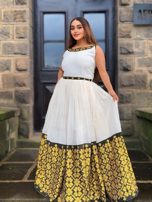 Woman wearing a white top with black and gold accents and a yellow patterned skirt, standing in front of a stone building.