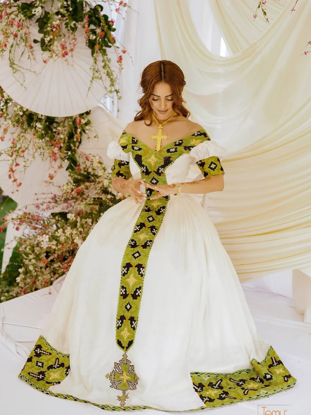 Woman in a white and green traditional outfit with floral decorations in the background