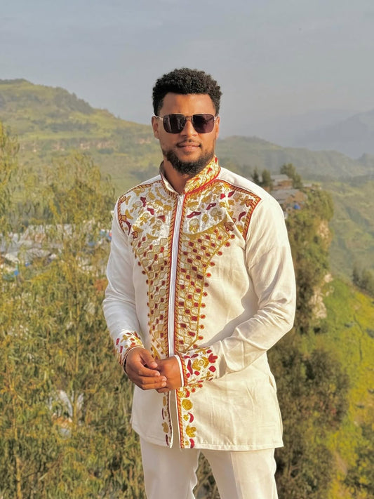 Man wearing a patterned jacket and sunglasses with a scenic background. Red & Gold Habesha Men's Shirt Ethgebya