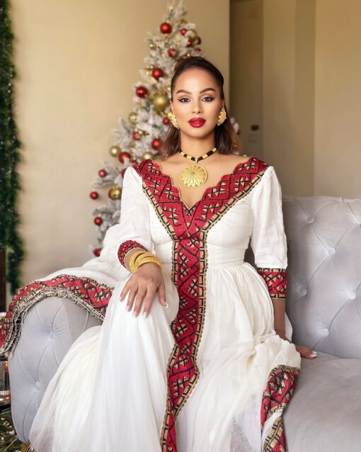 Woman in a white and red traditional outfit sitting on a couch with a decorated Christmas tree in the background.