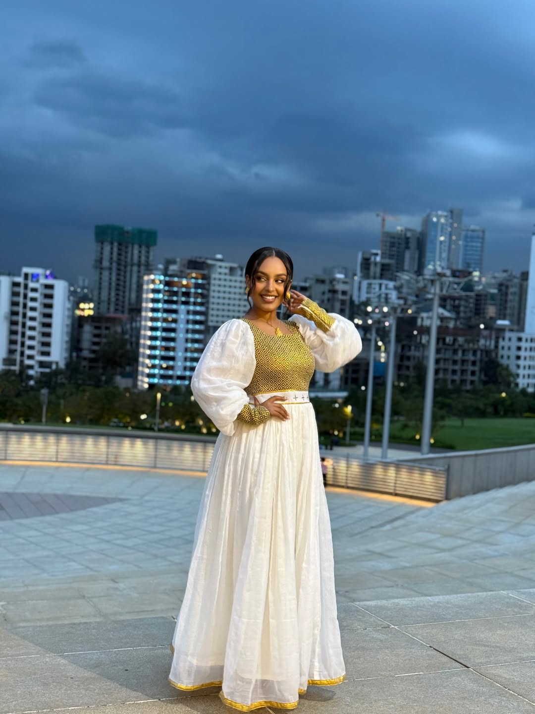 Woman in traditional outfit with cityscape in the background Gold Zuria Habesha Kemis New Elegant Modern Ethiopian Dress ethgebya gebeya habesha kemis