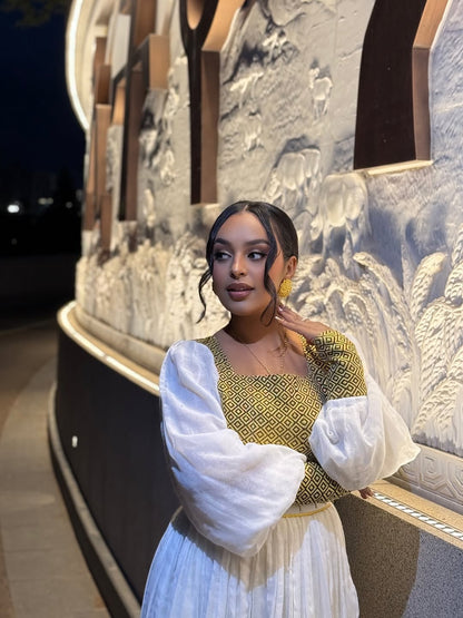 Woman in a yellow and white dress standing in front of an ornate architectural structure. Gold Zuria Habesha Kemis New Elegant Modern Ethiopian Dress ethgebya gebeya habesha kemis