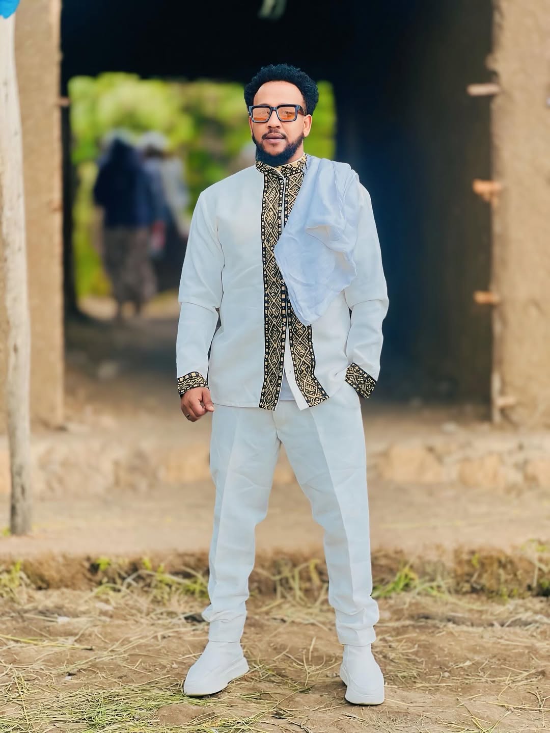 Man in formal attire standing outdoors with a rustic background Gold Habesha Men’s Shirt Modern Ethiopian Traditional Wear ethgebya gebeya