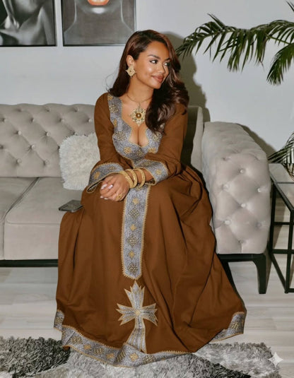 Woman in a brown dress with intricate patterns sitting on a couch in a living room. Brown Dominant Zuria Habesha Kemis Modern Ethiopian & Eritrean Dress Ethiopia Gebeya Ethgebya
