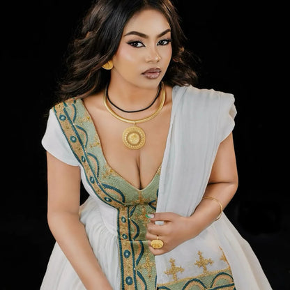 Woman wearing a traditional outfit with gold jewelry against a black . Green & Gold Zuria Habesha Kemis Ethgebyabackground