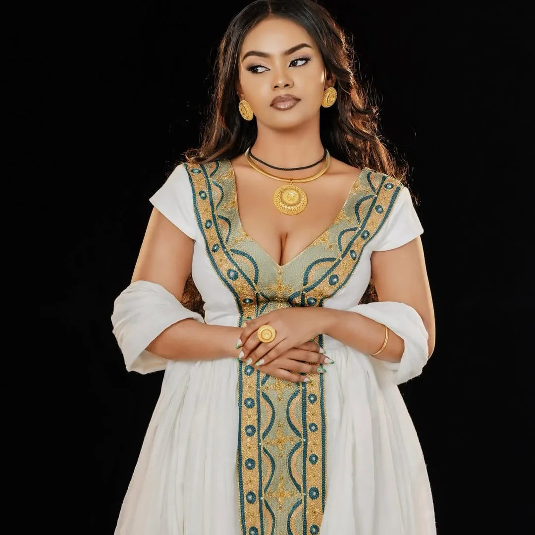 Woman wearing a traditional outfit with intricate designs and jewelry against a black background. Green & Gold Zuria Habesha Kemis Ethgebya