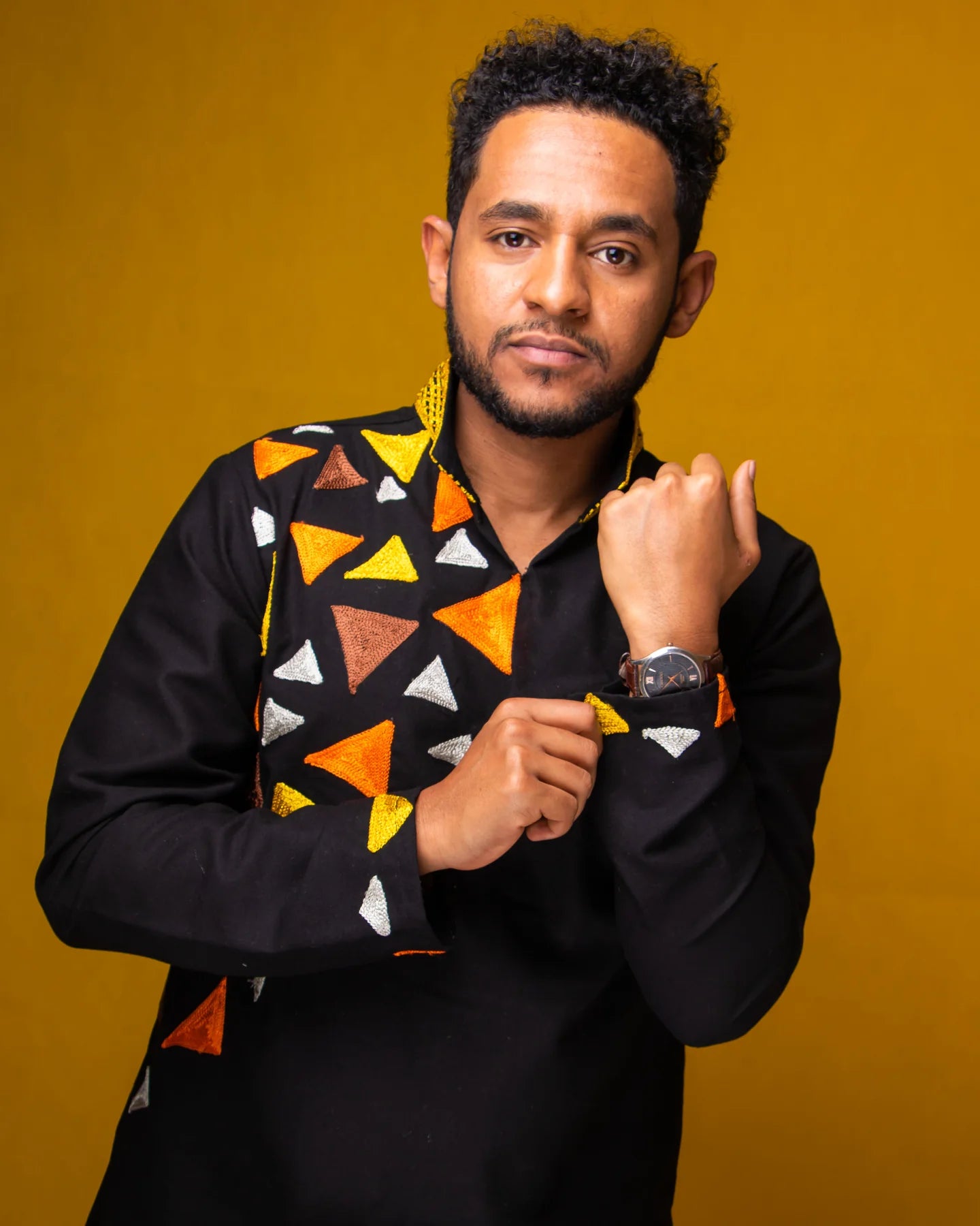 Man wearing a black shirt with colorful geometric patterns against a mustard yellow background