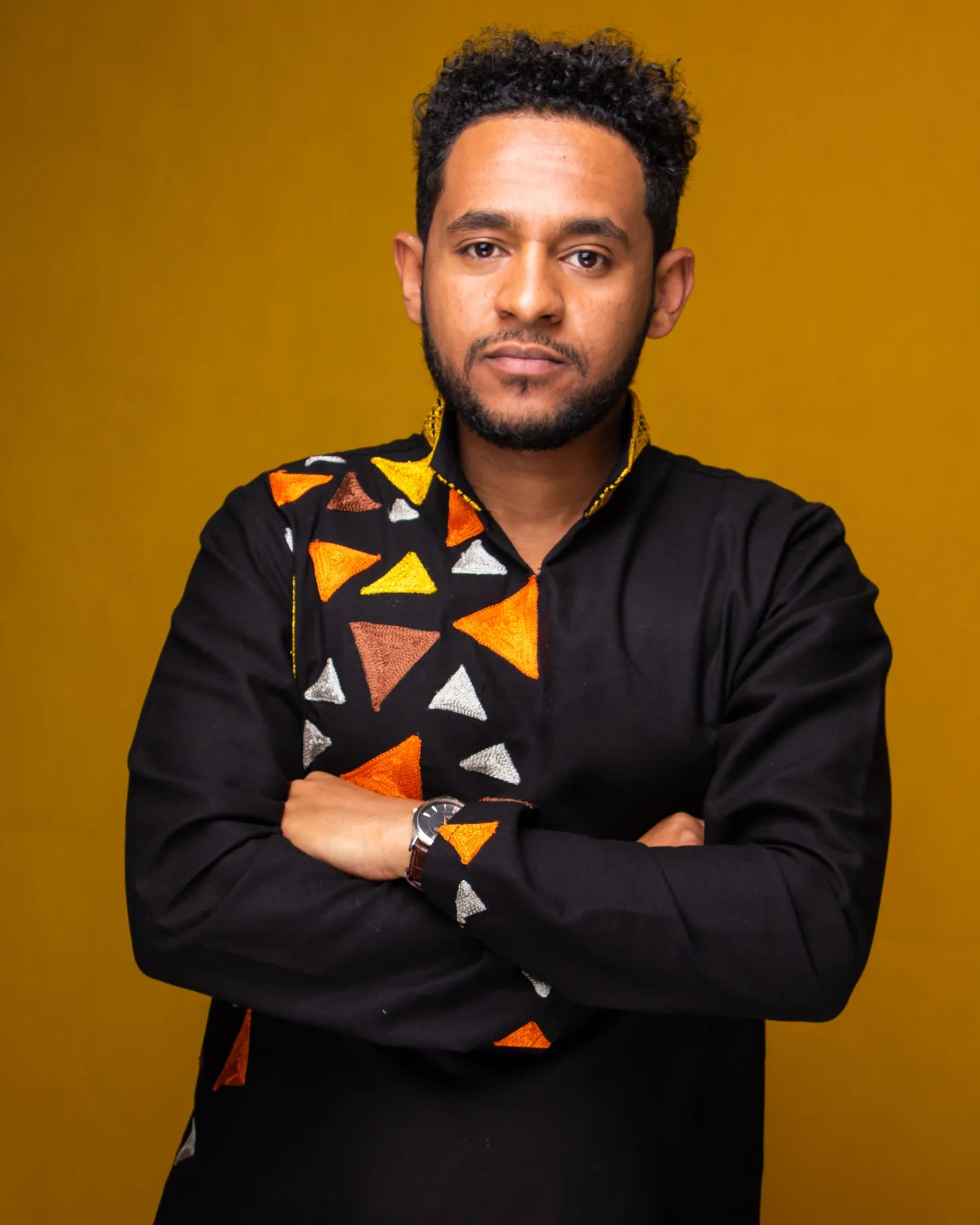 Man wearing a black shirt with colorful geometric patterns against a mustard yellow background