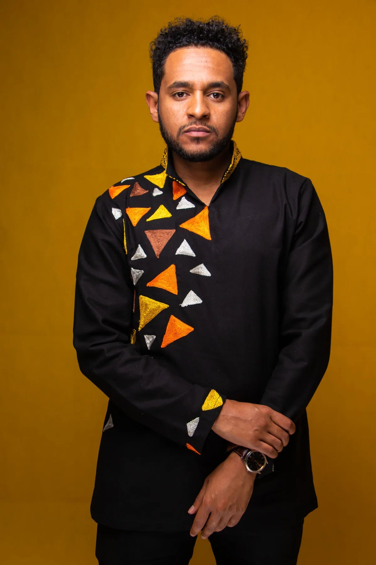 Man wearing a black shirt with colorful geometric patterns against a yellow background