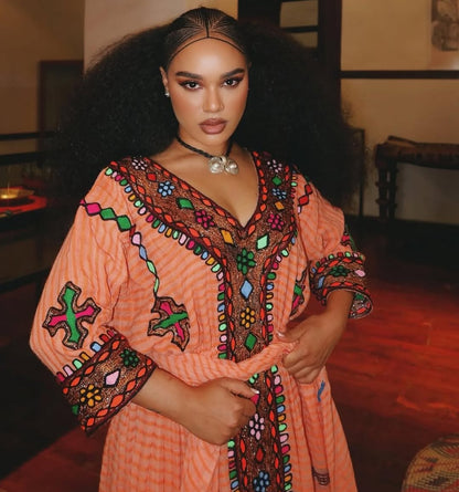 Woman wearing a colorful embroidered dress in an indoor  Gold Sand Ethiopian & Eritrean Axum Habesha Dress Ethgebyasetting