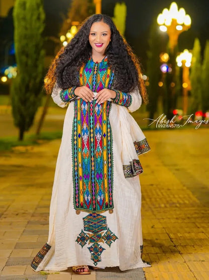 Woman in a colorful traditional outfit standing on a street at night.