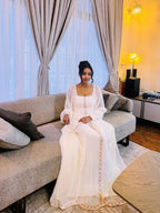 Woman in a white dress sitting on a gray sofa in a well-lit room. Long Sleeve Habesha Kemis | New Minimalist Ethiopian Traditional Dress ethgebya