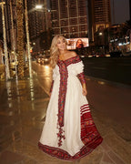 Woman in a white dress with red and gold embroidery standing on a city street at night. Red Zuria Habesha Kemis | Handcrafted Ethiopian & Eritrean Fetil Dress Ethgebya