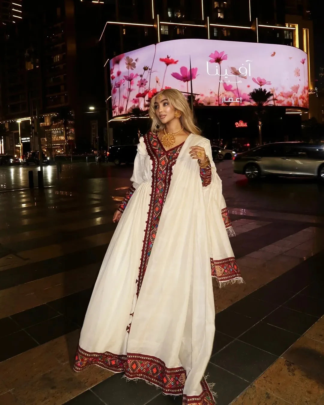 Woman in a white embroidered dress standing on a city street at night. Red Zuria Habesha Kemis | Handcrafted Ethiopian & Eritrean Fetil Dress Ethgebya