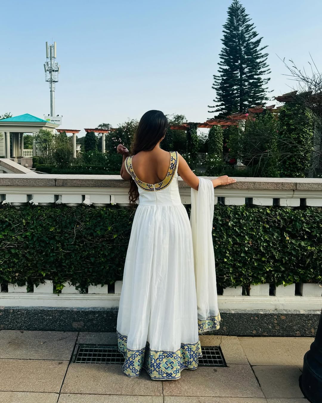 Woman in a white traditional outfit with floral patterns standing outdoors.Luxury Navy, Gold & Green Zuria Kemis