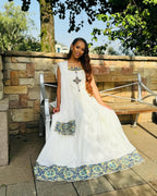 Woman in a white dress with floral patterns sitting outdoors on a stone patio. Luxury Navy, Gold & Green Zuria Kemis