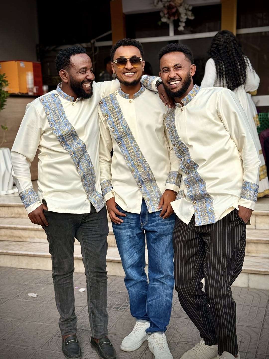 Three men in matching outfits with decorative sashes standing together outdoors. Modern Habesha Shirt for Men New Ethiopian Cultural Tilet Clothing Ethgebya