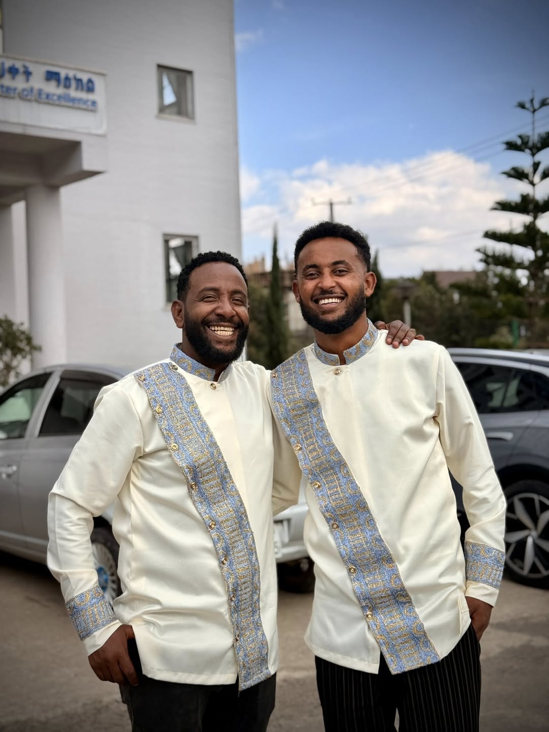 Two men in matching white jackets with blue accents standing outdoors. Modern Habesha Shirt for Men New Ethiopian Cultural Tilet Clothing Ethgebya