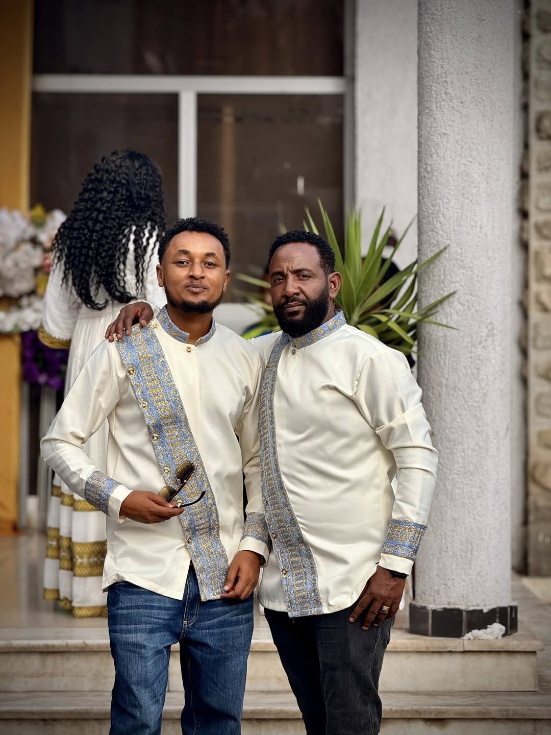 Two men in formal attire standing outdoors with a building and plants in the background Modern Habesha Shirt for Men New Ethiopian Cultural Tilet Clothing Ethgebya