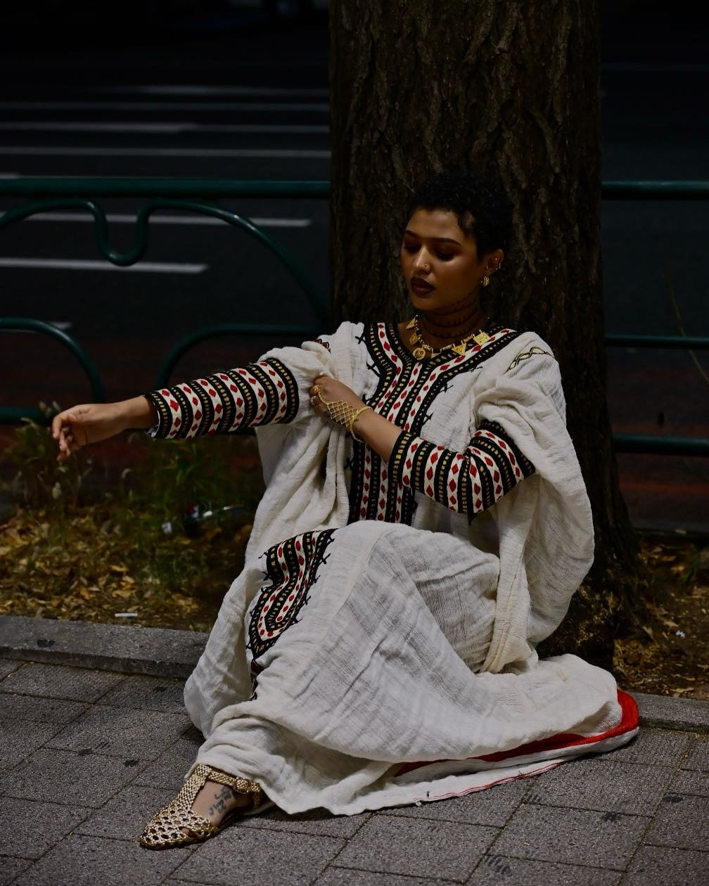 Woman in traditional outfit sitting on a bench outdoors. New Gondar Habesha Kemis Classic Ethiopian Traditional Dress Ethiopia Gebeya Ethgebya