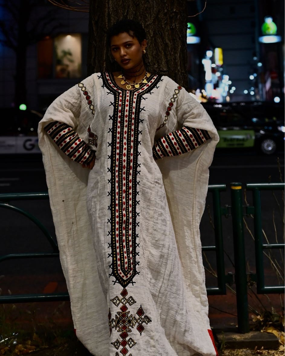 Woman wearing a long, embroidered white dress with intricate patterns in an urban setting. New Gondar Habesha Kemis Classic Ethiopian Traditional Dress Ethiopia Gebeya Ethgebya