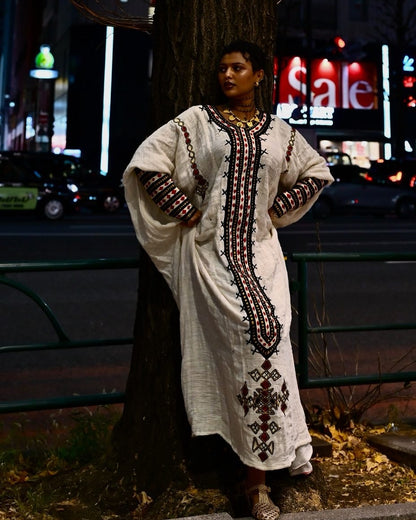 Person wearing a long, embroidered dress standing on a street at night. New Gondar Habesha Kemis Classic Ethiopian Traditional Dress Ethiopia Gebeya Ethgebya
