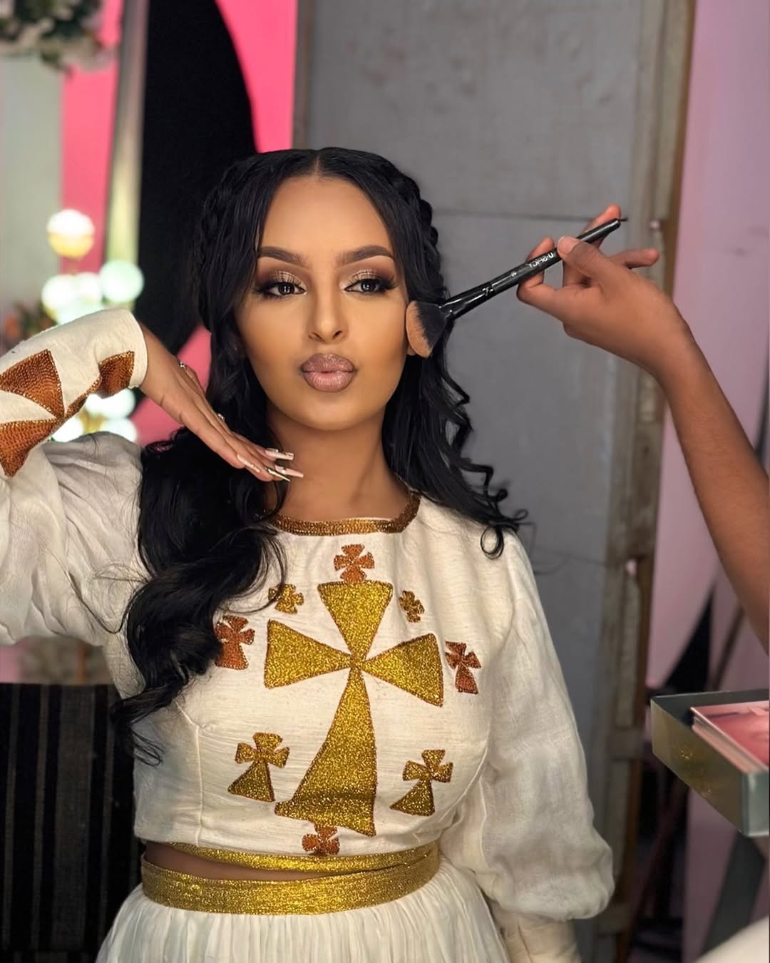 Woman getting makeup applied with a brush, wearing a white and gold traditional outfit. Golden Ethiopian Habesha Dress Handcrafted Zuria Kemis Set ethgebya gebeya usa zuria habesha kemis 