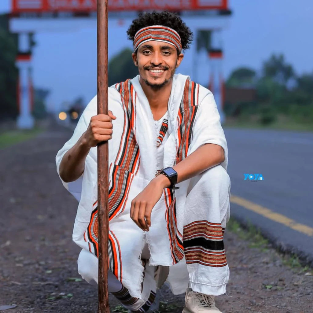 Man in traditional attire holding a pole on a road. Oromo Men’s Traditional Clothes Ethiopian Cultural Men's Woya Outfit Ethgebeya