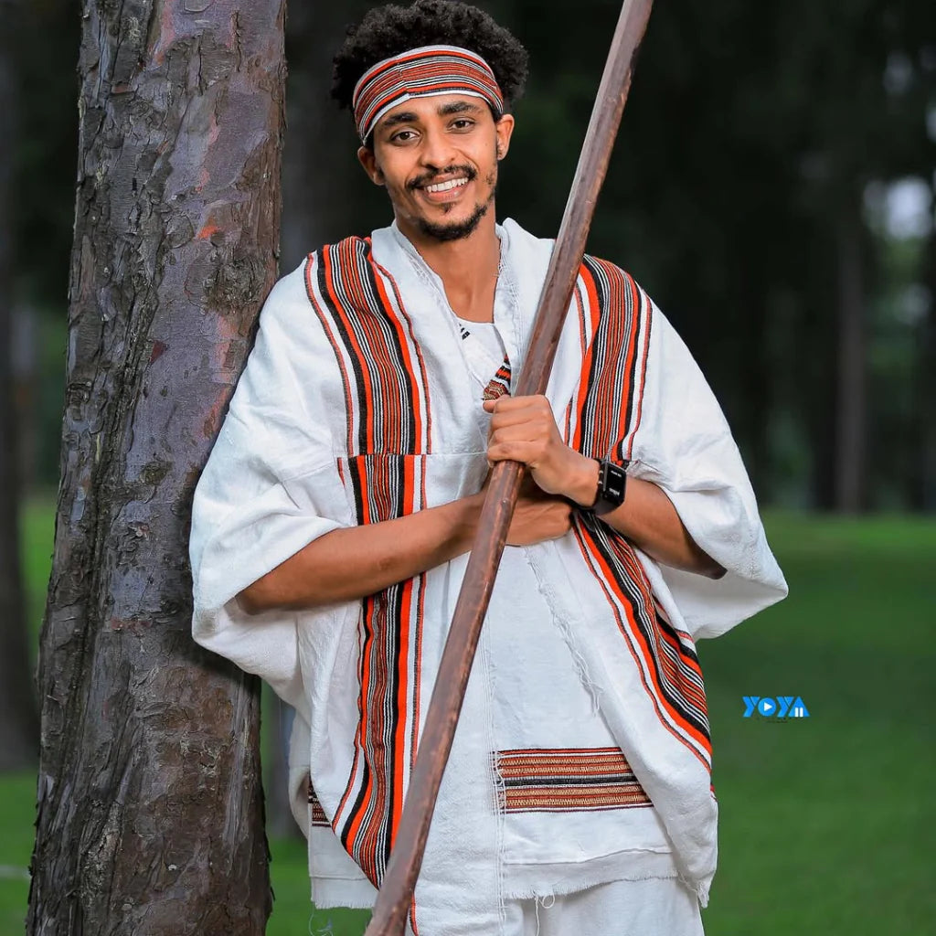Man in traditional attire holding a staff against a natural background Oromo Men’s Traditional Clothes Ethiopian Cultural Men's Woya Outfit Ethgebeya