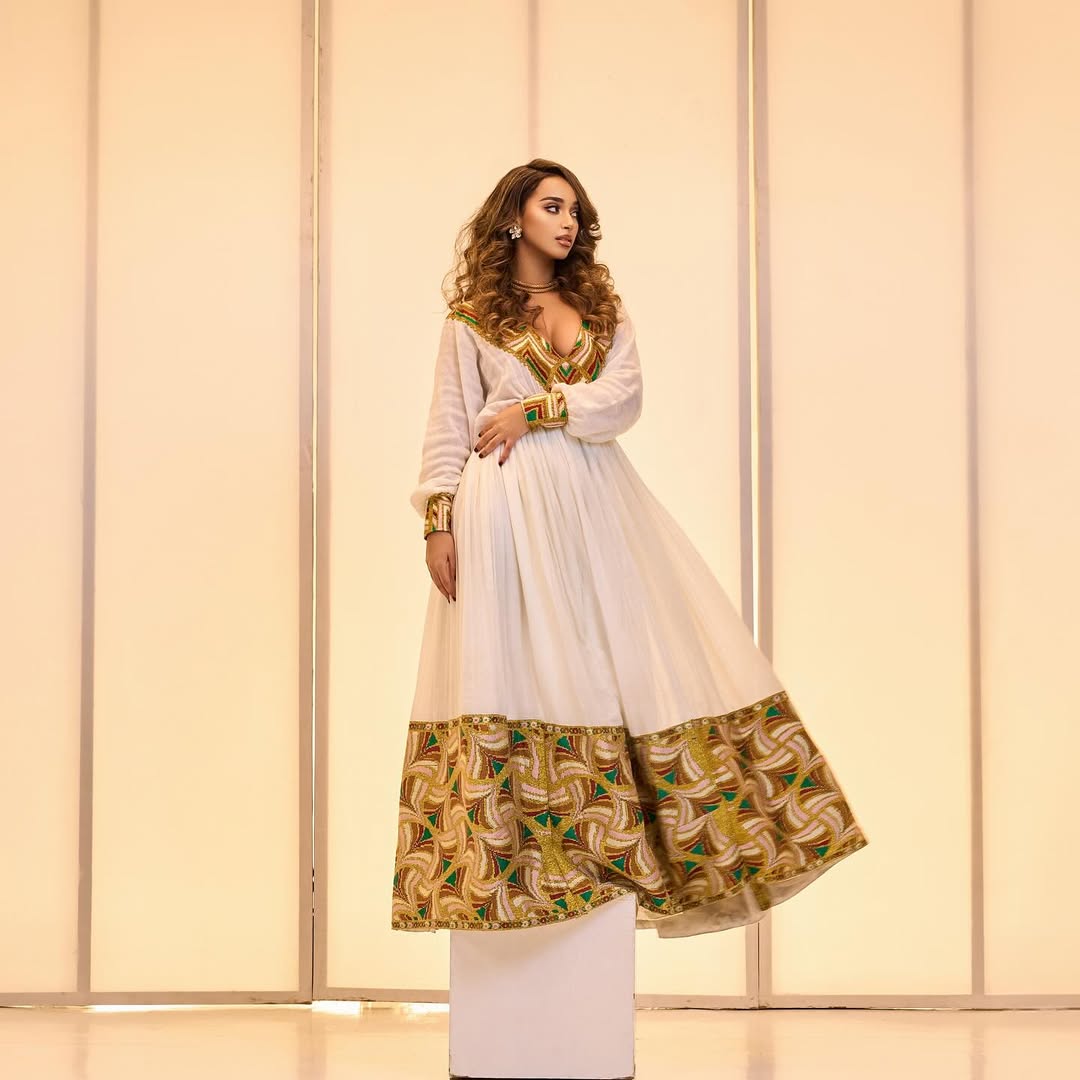 Woman wearing a traditional outfit with a white top and patterned skirt against a neutral background. Golden & Green Modern Zuria Habesha Kemis Ethiopian Traditional Dress ethgebya gebeya