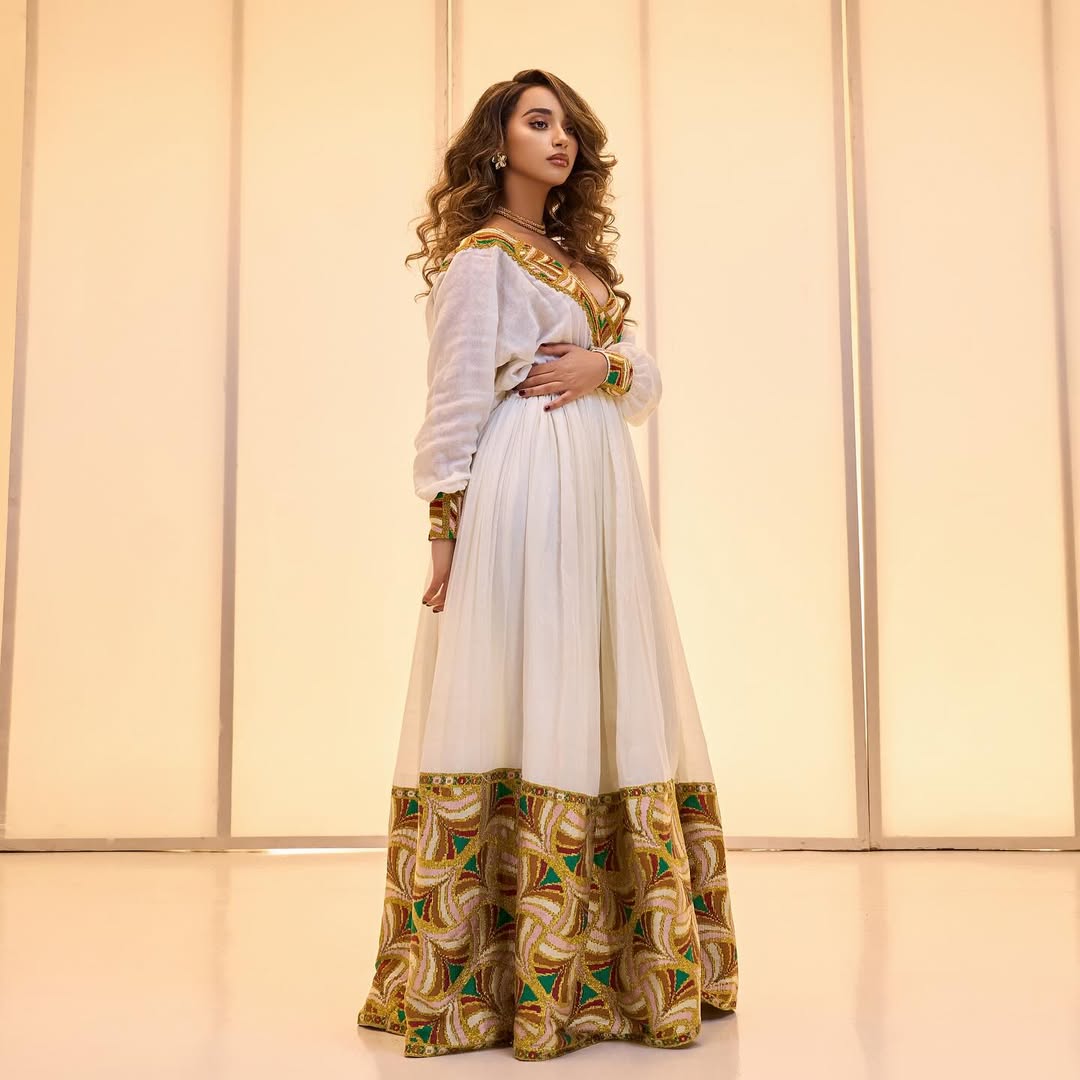 Woman wearing a white and gold traditional outfit with a patterned skirt against a light background Golden & Green Modern Zuria Habesha Kemis Ethiopian Traditional Dress ethgebya gebeya