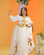 Woman in a white dress with gold and brown patterns against an orange background Golden Ethiopian Habesha Dress Handcrafted Zuria Kemis Set ethgebya gebeya usa zuria habesha kemis 
